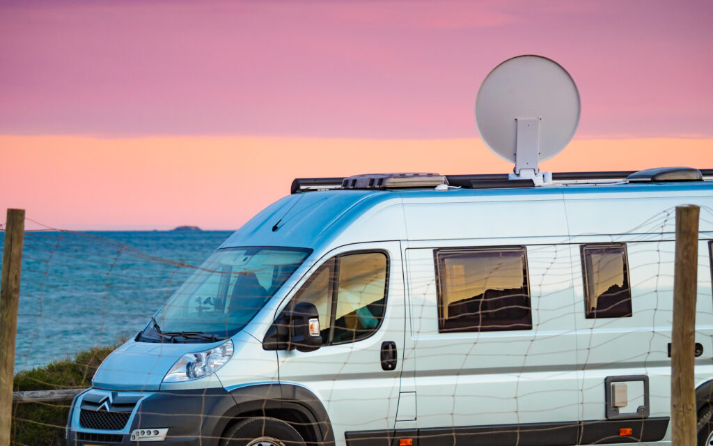 Wohnmobil mit Satellitenschüssel an der Küste bei Sonnenuntergang